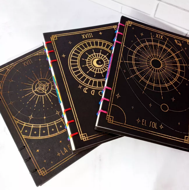cuadernos negros con diseños dorados de la estrella, la luna y el sol