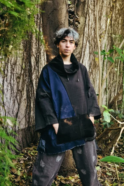 un modelo posa con una prenda parecida a un buzo, pero hecha con tela de jean color azul oscuro y negro con detalles en cuello y bolsillo de corderoy negro